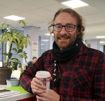 Staff image of a man holding a coffee, in an office setting